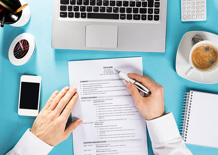 Image of a table with a laptop, phone, coffee and someone working on a document