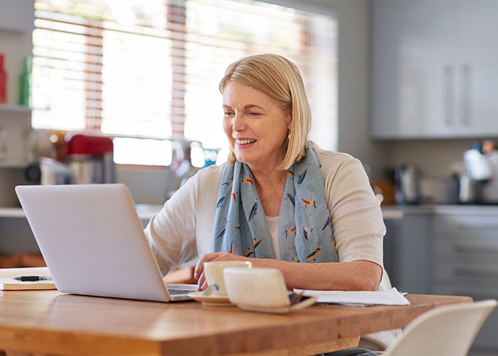 Image of woman sitting at her kitchen table, looking at a laptop